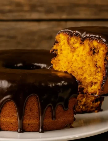 Imagem de um pedaço de bolo de cenoura com cobertura de chocolate,sendo servido.